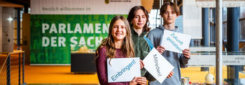 Drei Jugendliche stehen im Bürgerfoyer des Landtags mit Schildern, die dazu auffordern, aktiv zu werden.